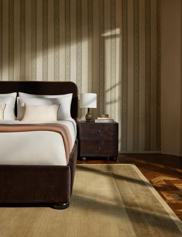 #color::ivy | A velvet upholstered platform bed and nightstand sit infront of a wall featuring the Paradiso striped Wallpaper by Jake Arnold